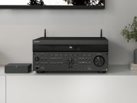 A Sony AV receiver with detailed controls, placed on a white cabinet next to a media device and greenery.